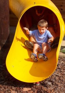 Boy going down playground slide with adult