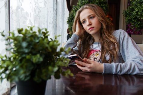 Sad teen girl holding smartphone
