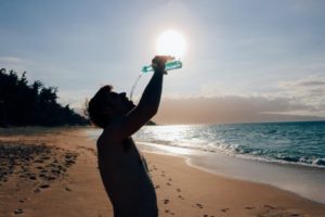 Man drinking water on beach in hot sun