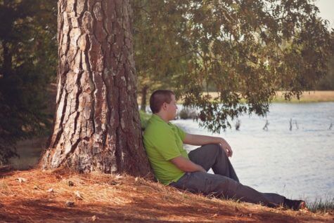 Man sitting alone next to a tree