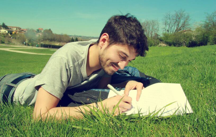 Man lying in grass writing