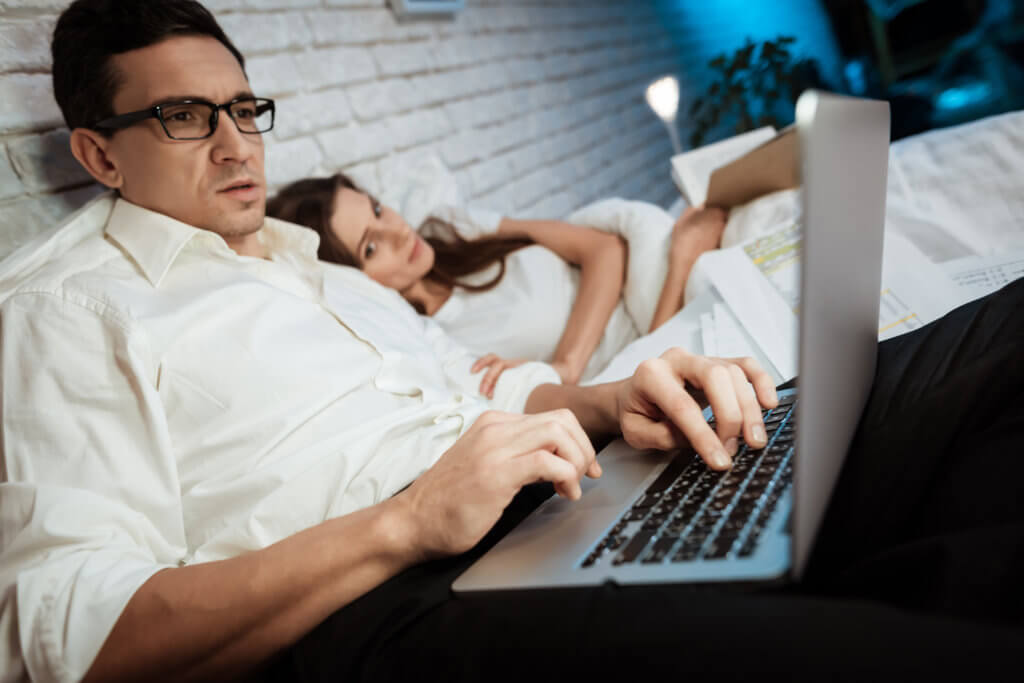 Man working on computer in bed with wife