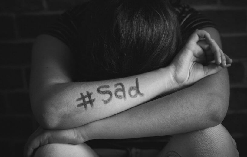 Upset person alone with "#sad" on arm