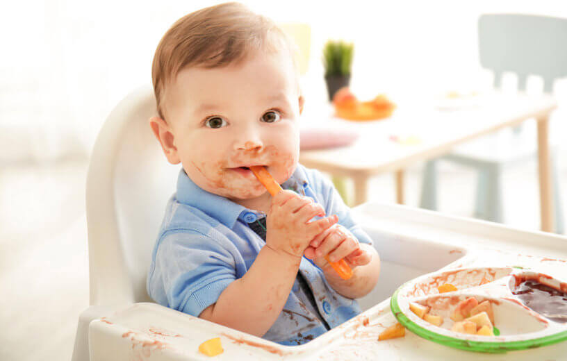 Cute messy baby eating puree at home in his high chair