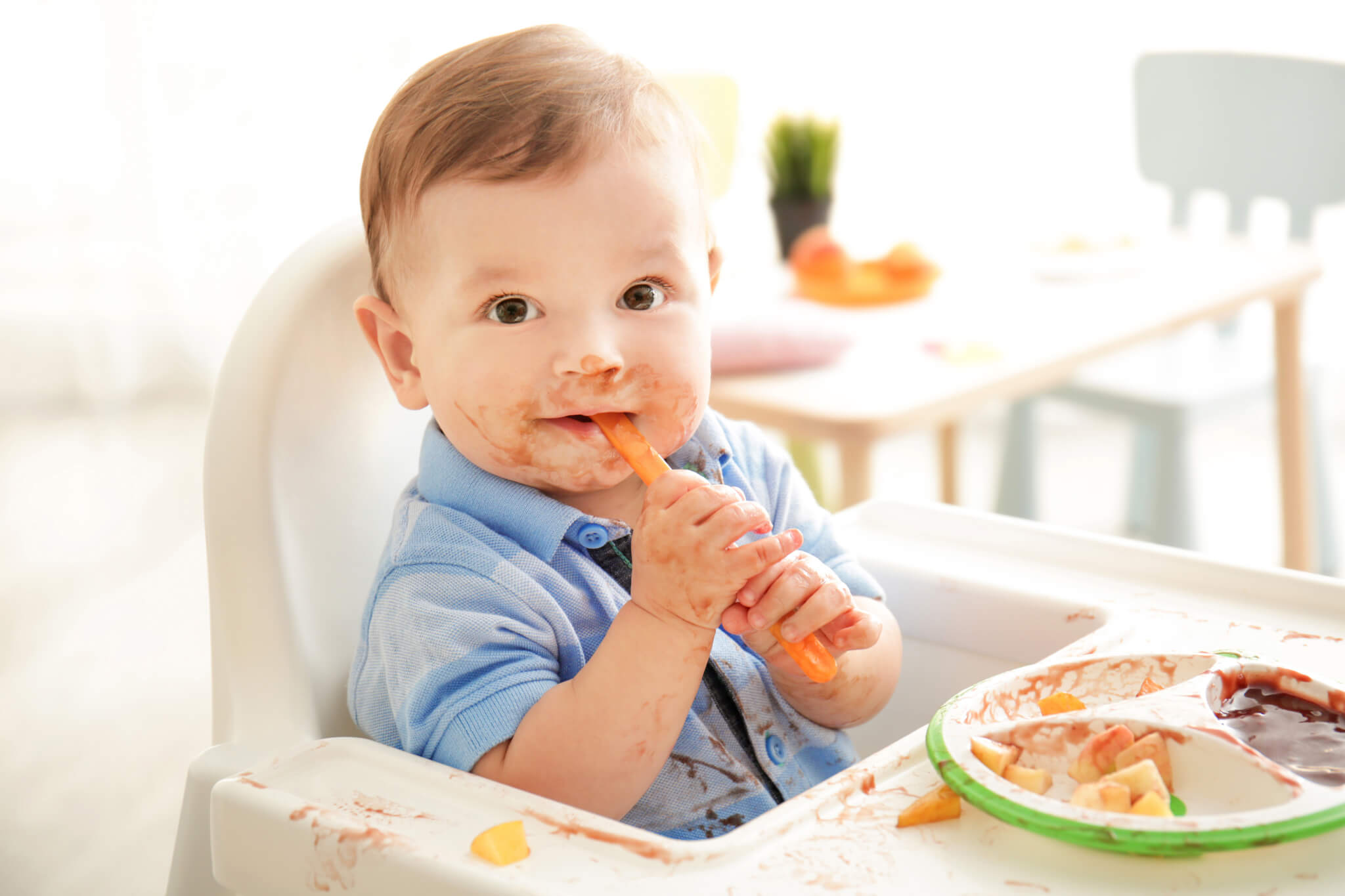 Cute messy baby eating puree at home in his high chair