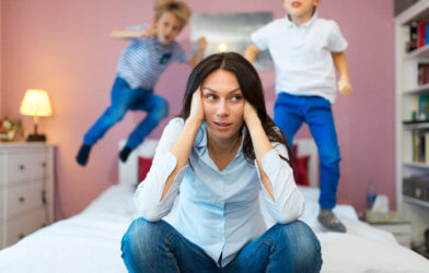 Tired, frustrated mother with children jumping on bed