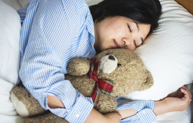A woman sleeping in bed with a teddy bear