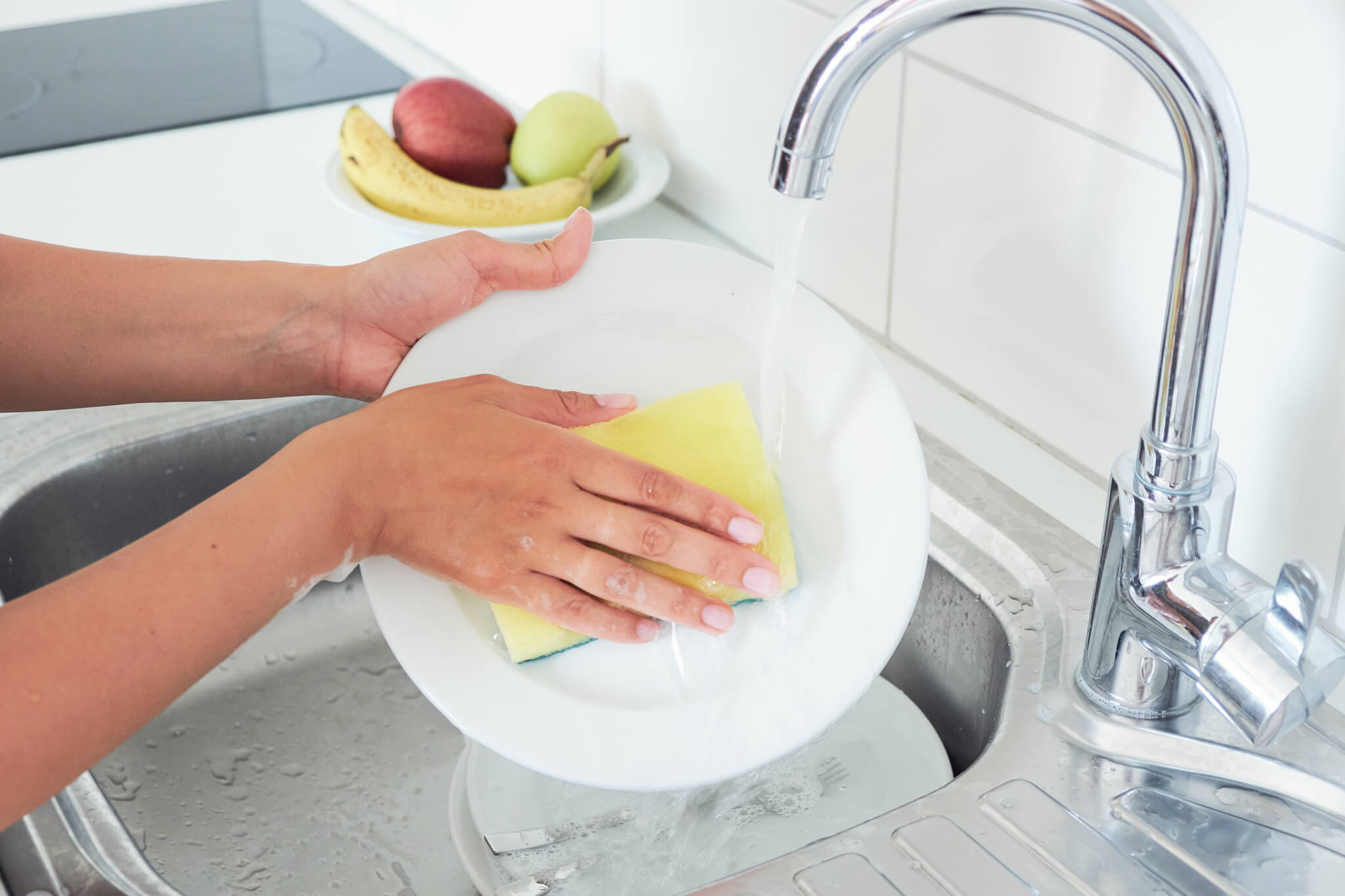 Person washing dishes with sponge in kitchen sink