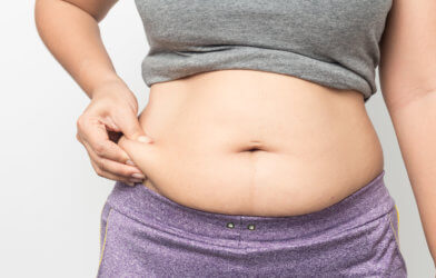 Overweight woman hand pinching excessive belly fat