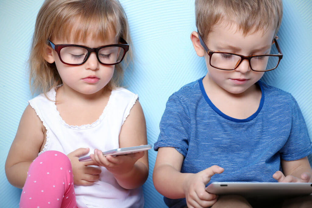 Young children wearing glasses while looking at smartphone, tablet screens