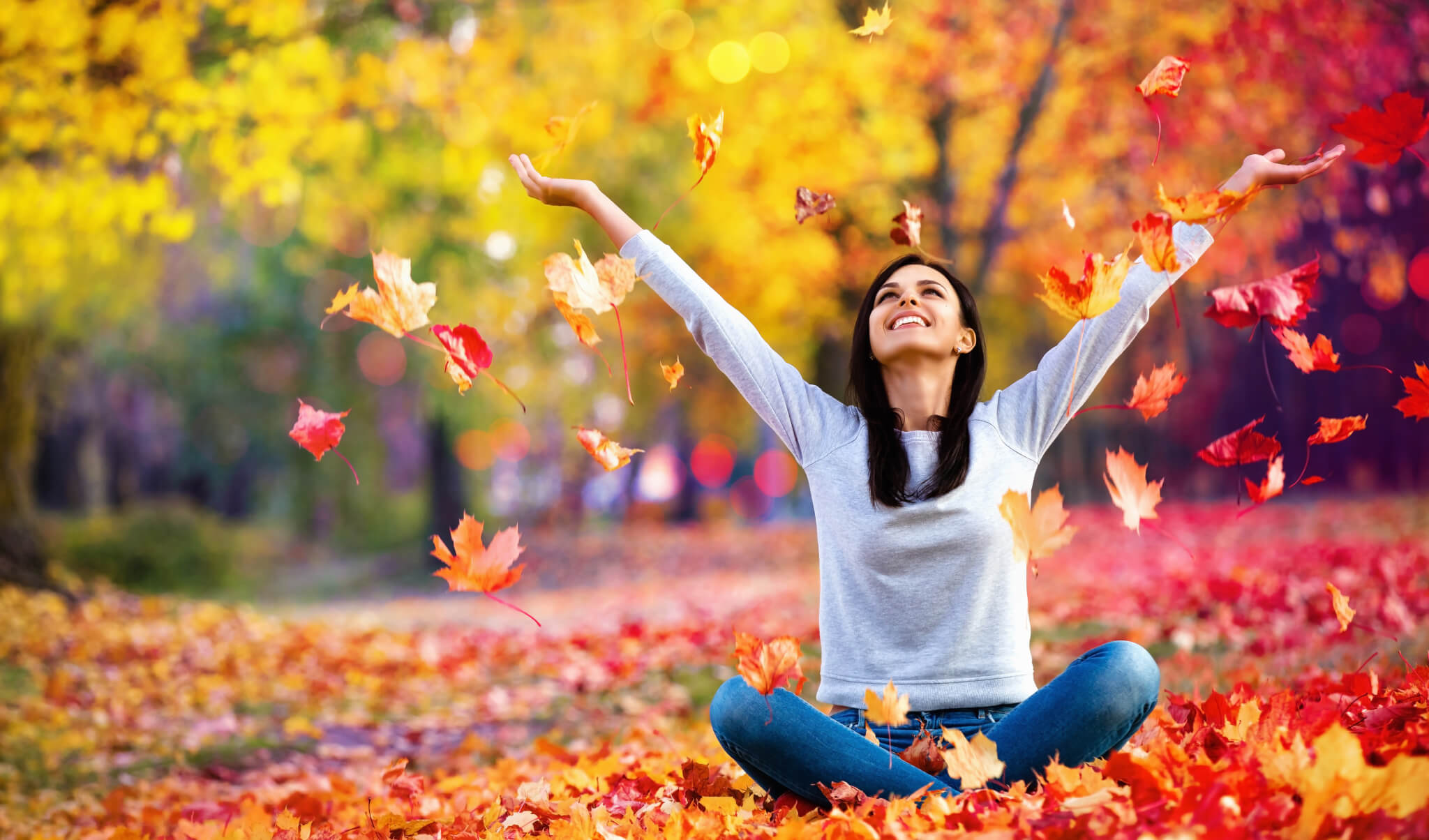 Happy woman throwing autumn leaves in the park
