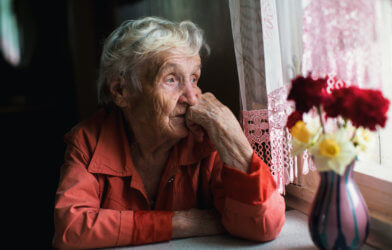 Sad, lonely elderly woman looking out window
