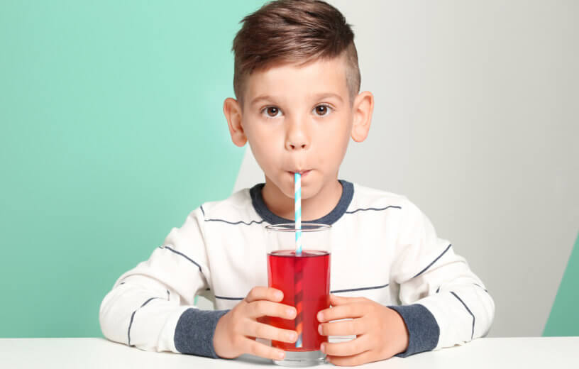 Boy drinking fruit juice or sugary drink in glass