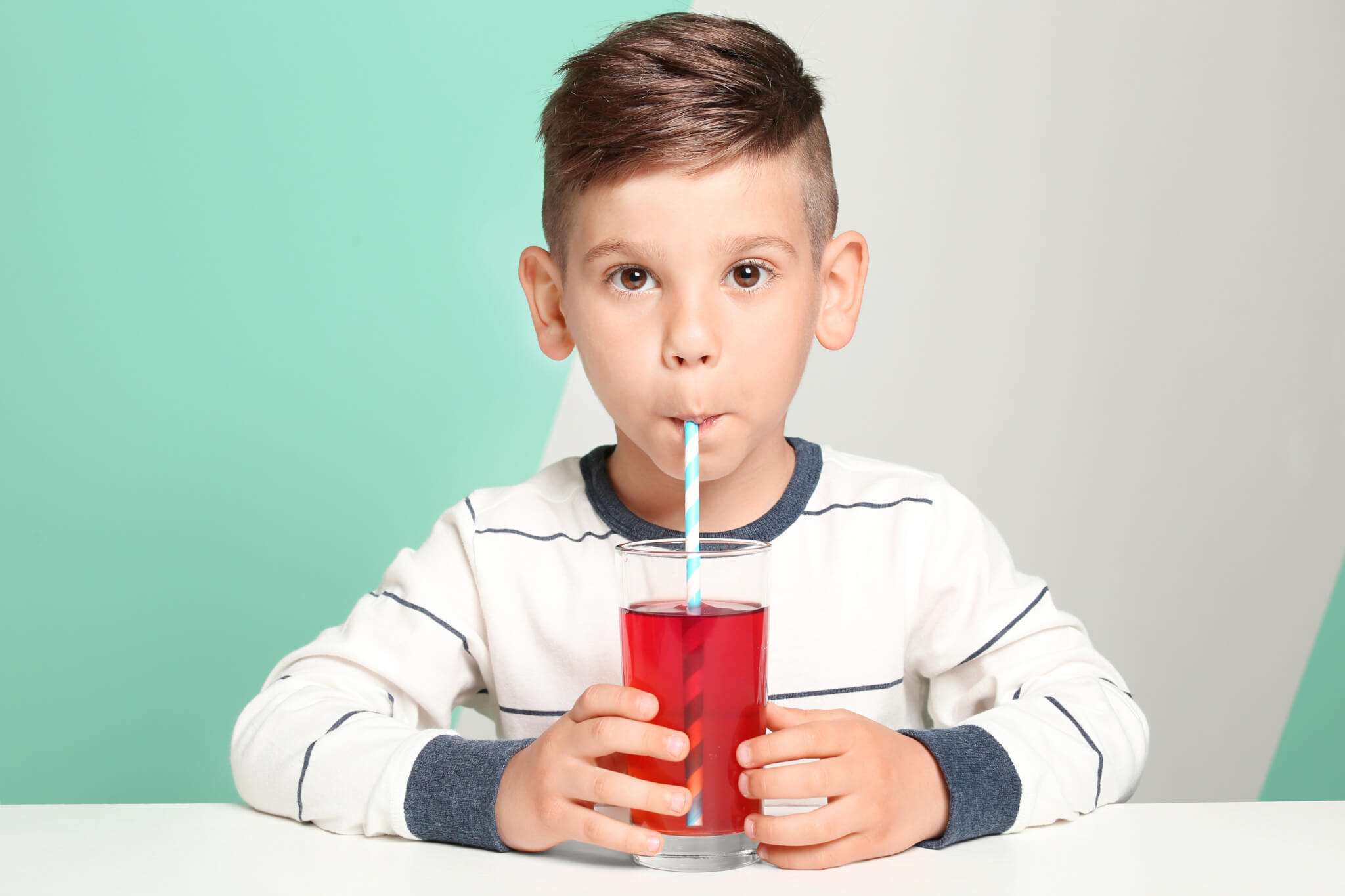 Boy drinking fruit juice or sugary drink in glass