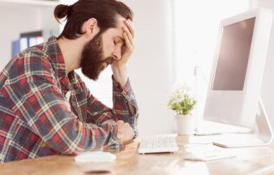Stressed, upset millennial sitting at work computer