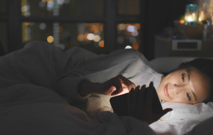 Woman looking at phone in bed, blue light in face