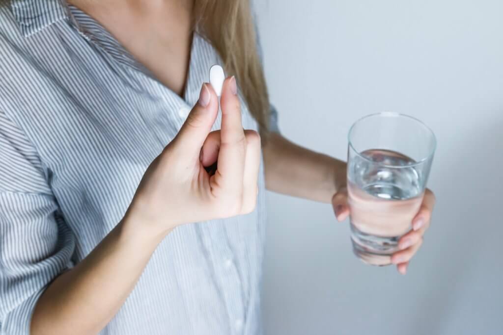 Woman holding pill, glass of water