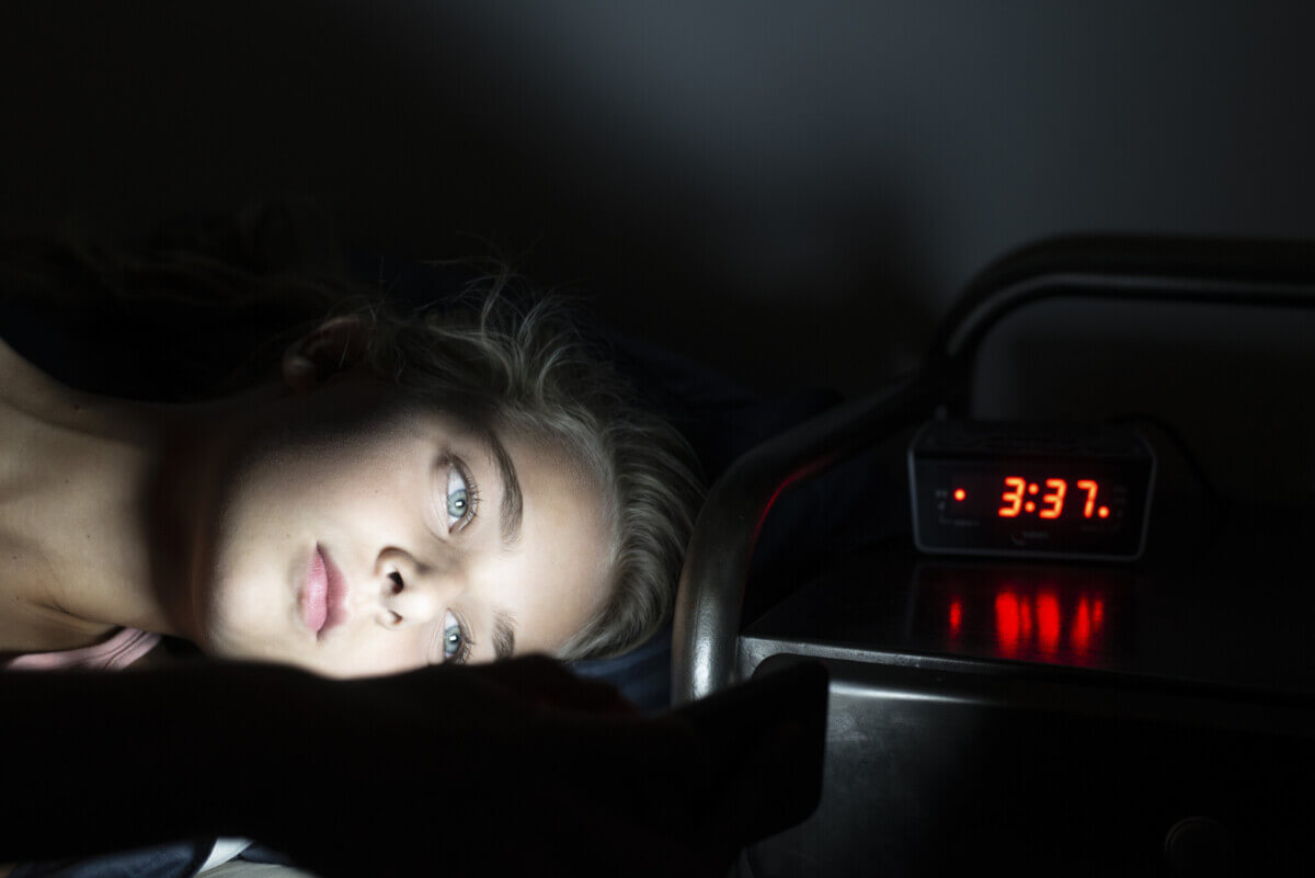 Young girl using mobile phone in bed at midnight, can’t sleep