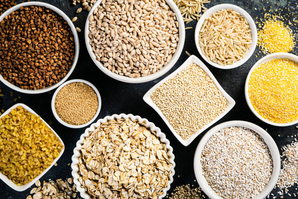 Selection of whole grains in white bowls - rice, oats, buckwheat, bulgur, porridge, barley, quinoa, amaranth