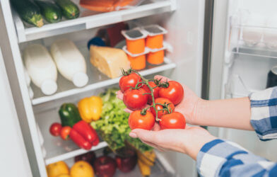 Woman holding tomatoes in front of refrigerator