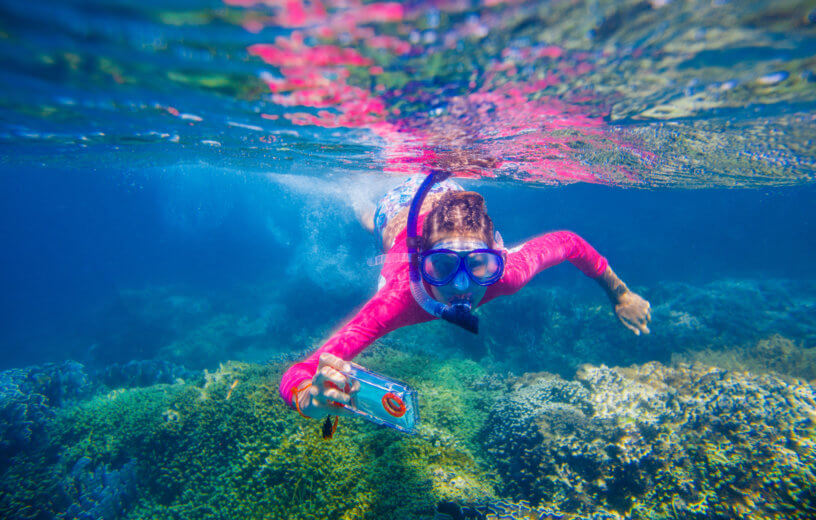 Girl or woman scuba diving with smartphone, taking selfie or streaming video underwater