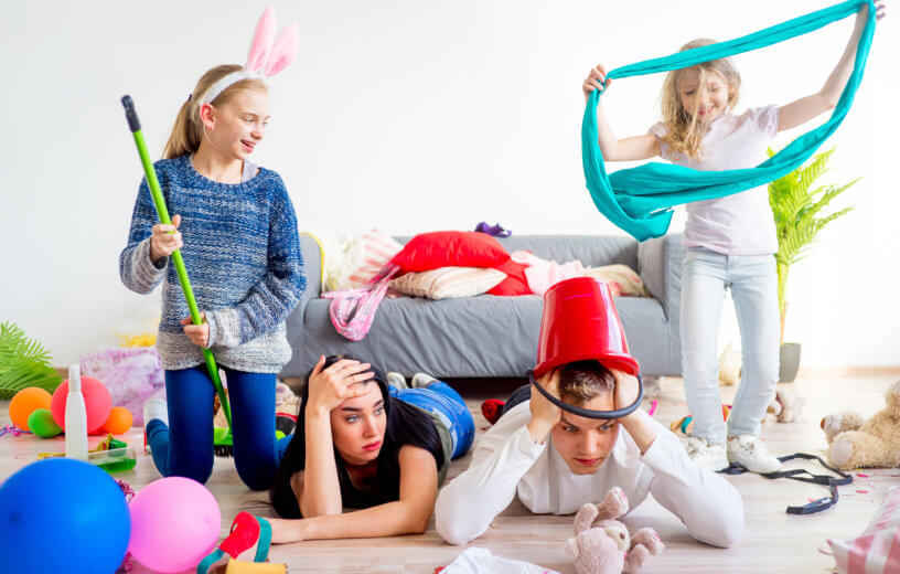 Stressed out, tired parents on floor with wild young children in messy home