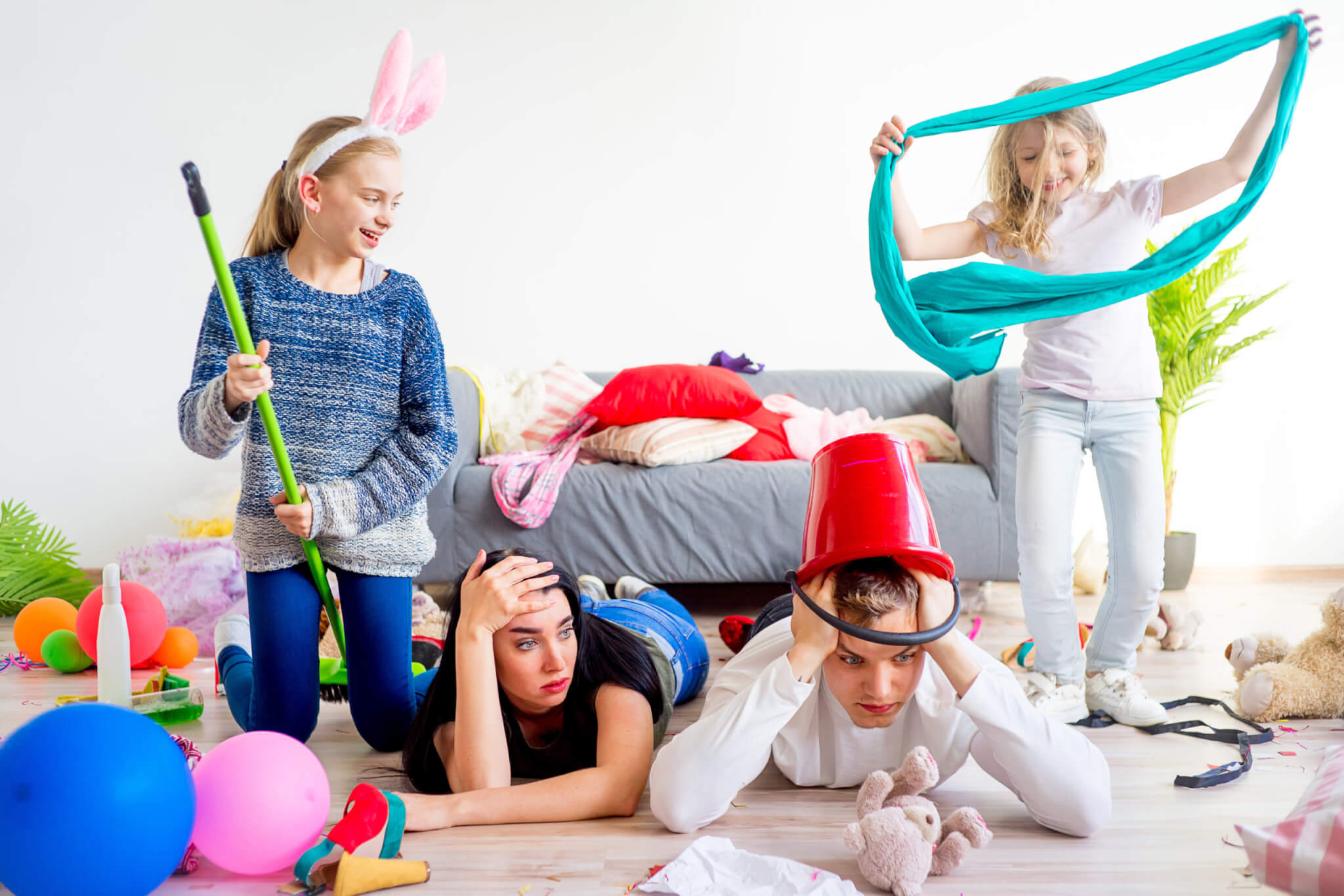 Stressed out, tired parents on floor with wild young children in messy home