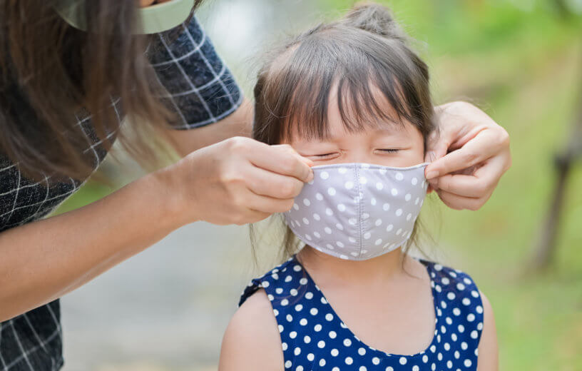 Mother putting a cloth mask on her child during the COVID-19 / coronavirus pandemic