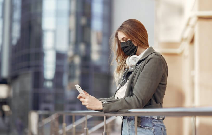 Woman wearing face mask while texting on phone during COVID-19 / coronavirus outbreak