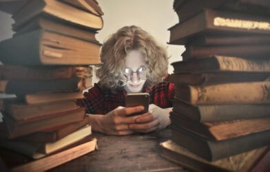 Teen looking at smartphone surrounded by books