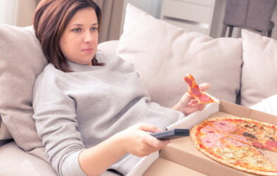 Woman eating pizza on the couch while watching TV
