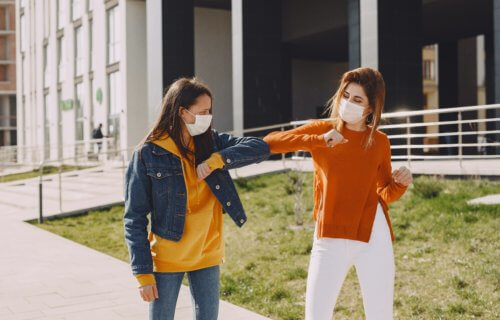 Women in masks elbow-bumping and social distancing during coronavirus pandemic