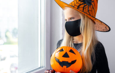 Young girl in face mask staying home for Halloween due to coronavirus / COVID-19