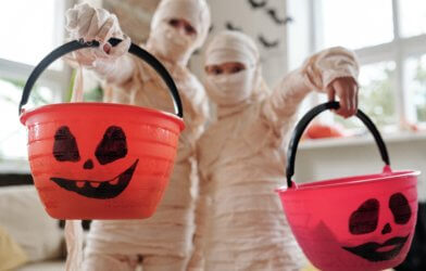 Children in Halloween mummy costumes with trick-or-treat candy buckets
