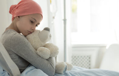Young girl with cancer hugging teddy bear