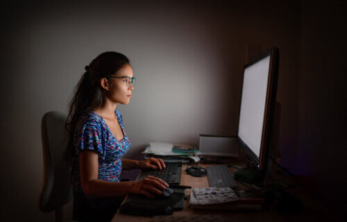 Woman wearing blue light glasses while doing work at night on computer