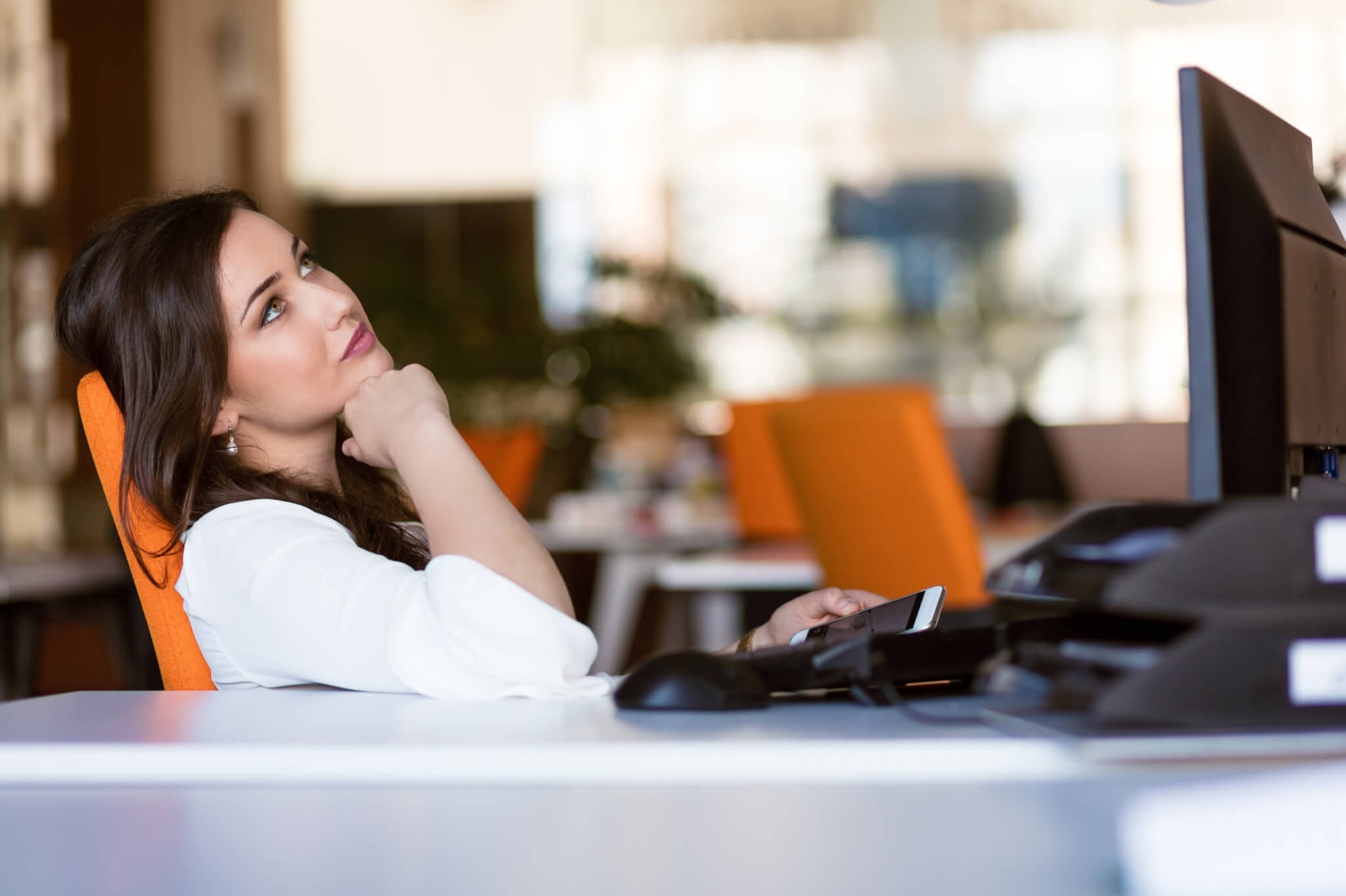 Woman sitting at office desk, daydreaming while working