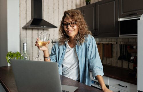 Woman drinking glass of wine on video chat with computer