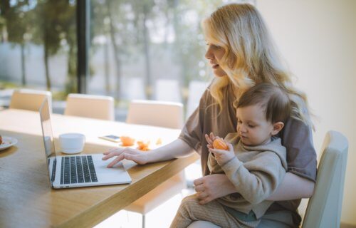 Mother holding child on lap while doing work on laptop
