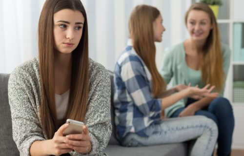 Sad or jealous girl holding phone while friends talk behind her back