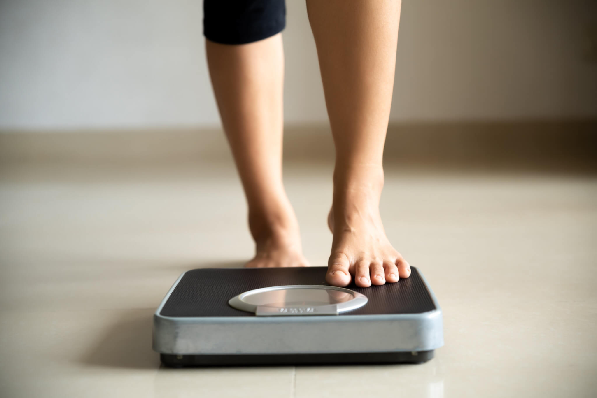 Woman stepping on scale, checking weight loss or weight gain