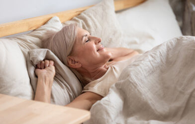 Older woman waking up in bed happy, rested from good night of sleep