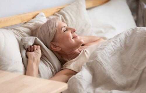 Older woman waking up in bed happy, rested from good night of sleep