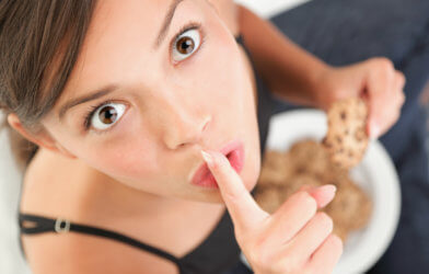 Woman eating cookie in secret, cheating on diet