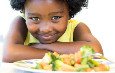 Cute little girl smiling while eating plate of vegetables
