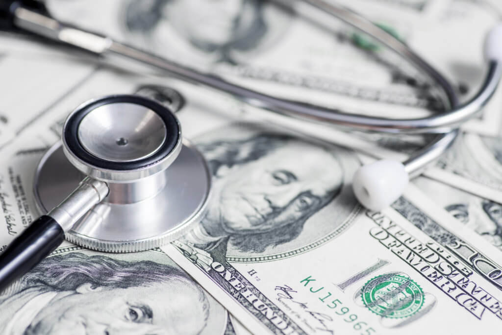 Wealth and health: Stethoscope on top of $100 bills, money