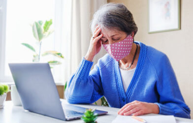 Woman in face mask experiencing COVID-19 symptoms while working