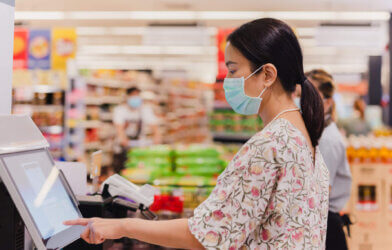 Woman in face mask using self-checkout line at grocery store