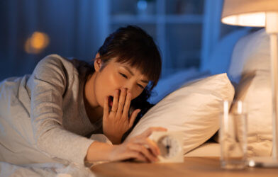 Woman tired, yawning in bed setting clock