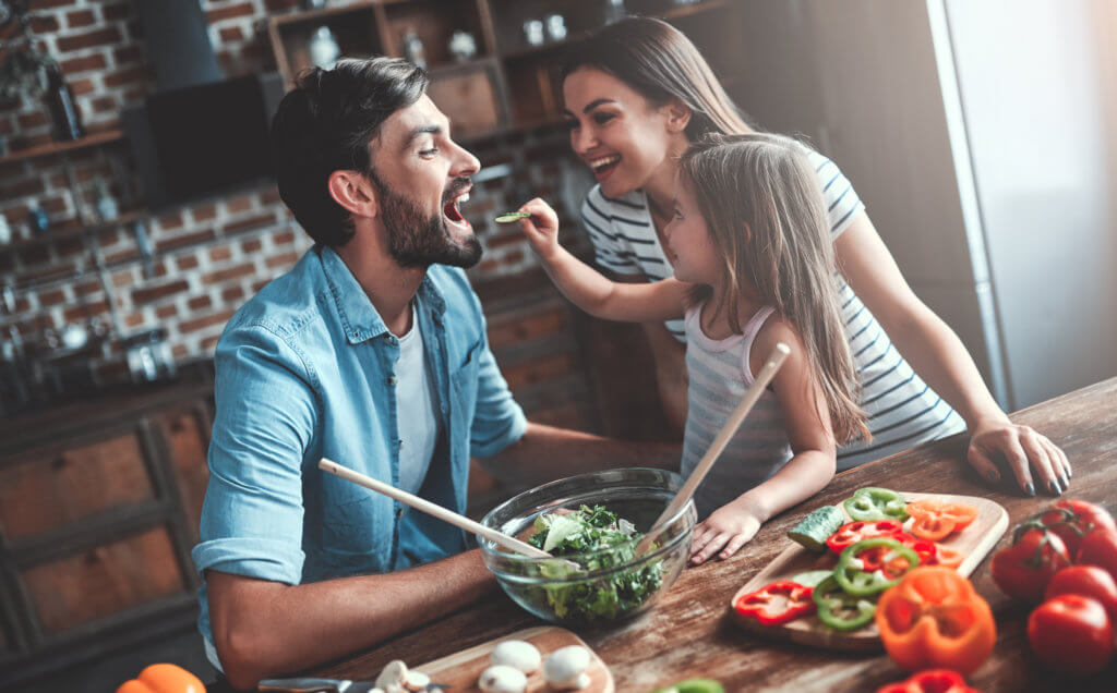 Little girl feeding her parents salad and vegetables